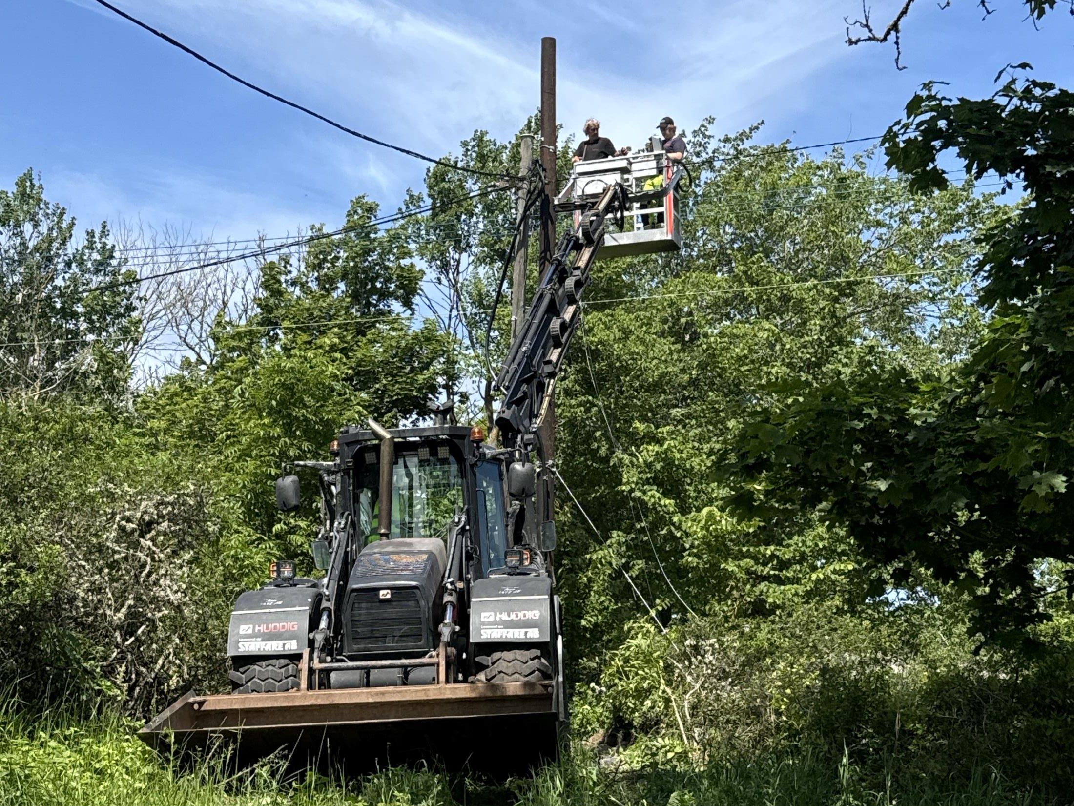 Maskin med lyftarm arbetar intill järnvägsspår i skogsmiljö